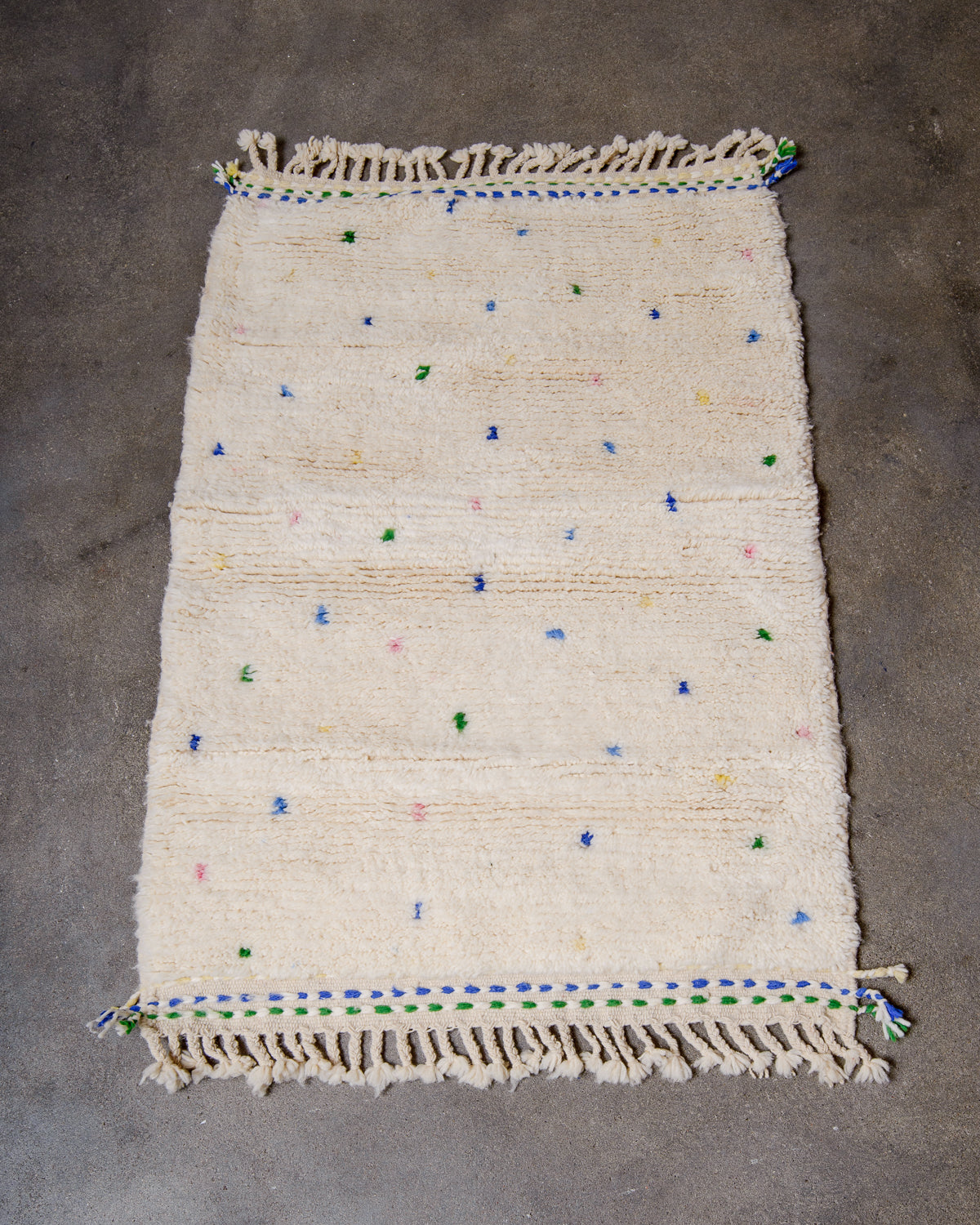 Berberlin Beniourain rug with coloured dots laying flat on concrete studio floor.